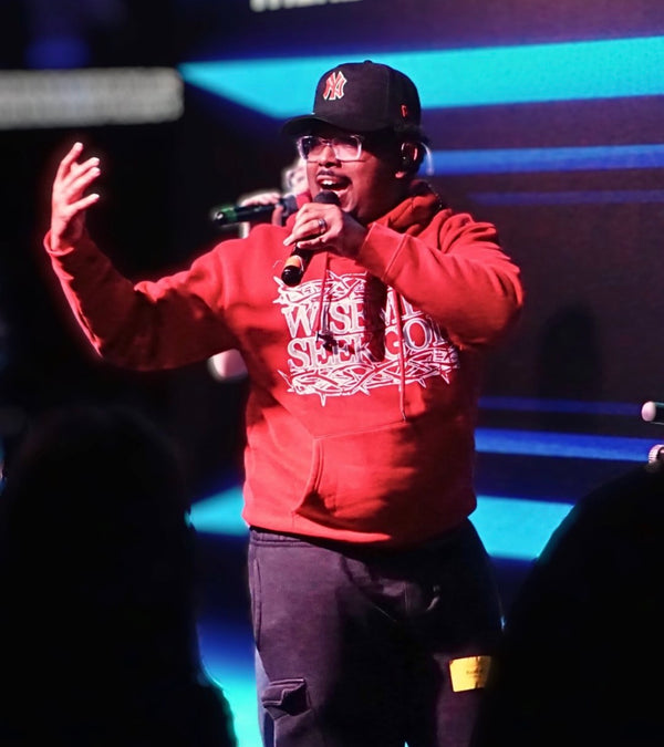 Person in a Wise Men Seek God hoodie on stage holding a microphone